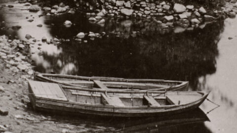 A coble sits on the shore of a river bank