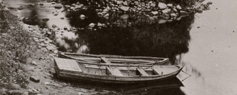 A coble sits on the shore of a river bank