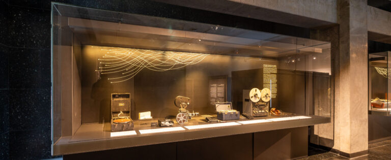 A display case with assorted fieldwork equipment including recorders, headsets and microphones.