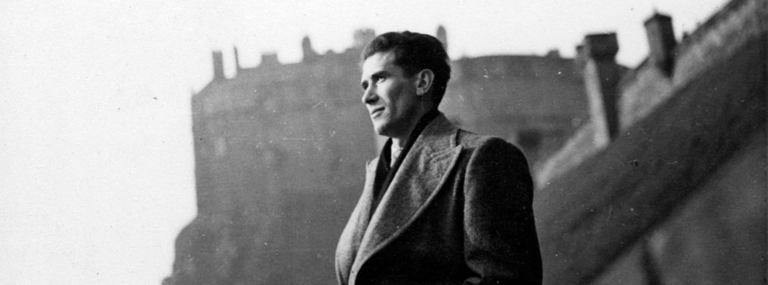 A black and white photograph with a man looking left in an overcoat in the foreground and Edinburgh Castle in the background.