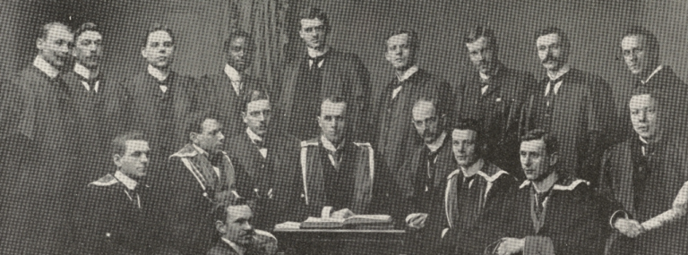 Scan of a page from an edition of The Student magazine published in 1898. The page contains a black and white photograph of the Students’ Representative Council Executive Committee of 1898 – 99. In the photograph, the Executive Committee of eighteen men are standing and sitting around a small table in the centre of the photograph, dressed in formal late nineteenth century dress, many wearing university gowns. Richard Akiwande Savage is standing in the row of men at the back of the photograph, fourth from the left. He is the only black man in the photograph. Under the photograph are printed the names of the Executive Committee members.